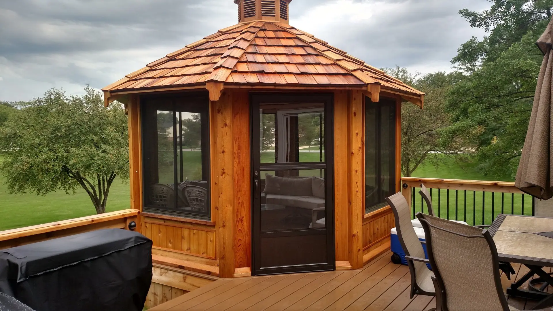 A wooden gazebo with a roof and windows.