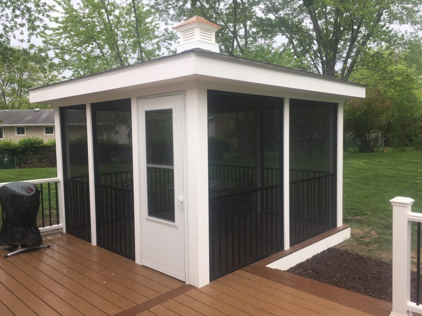 A white and black screened in porch with a wooden deck.